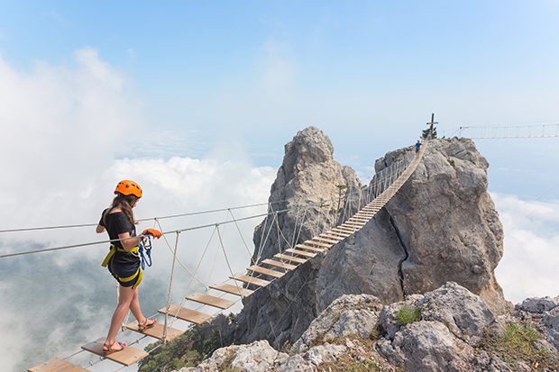 Young woman crossing the chasm on the rope bridge