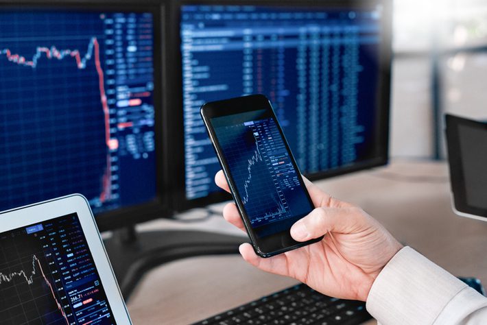 Stocks and Funds. Trader sitting at office in front of monitors with data using app on smartphone monitoring price changes close-up