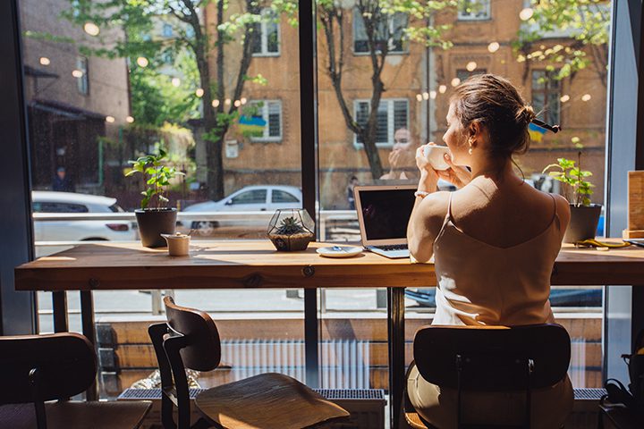 Caucasian romantic woman blogger relaxing drinking tea while sitting near the window in modern loft cafe bar,female freelancer thinking about new ideas during work on laptop computer. Copy space