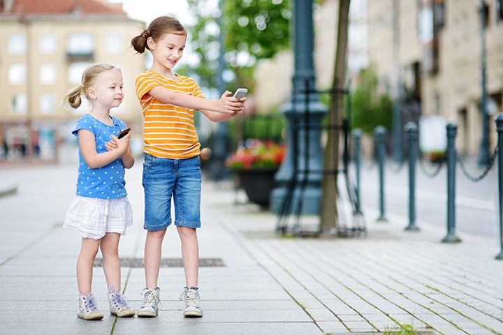 Two cute little sisters playing outdoor mobile game on their smart phones