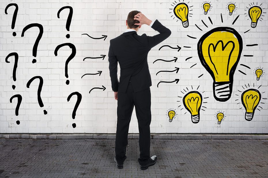 Confused Businessman Looking At Question Marks And Light Bulbs