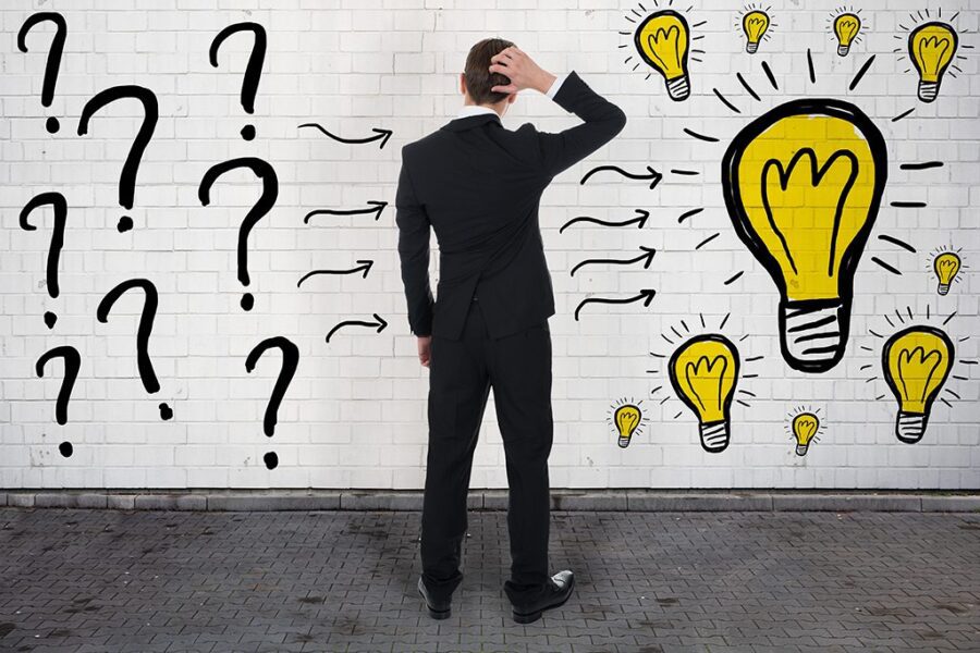 Rear view of confused businessman looking at question marks and light bulbs on wall