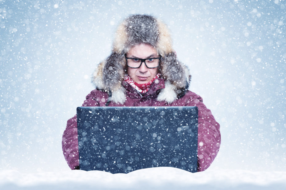 Frozen man in red winter clothes working on a laptop in the snow