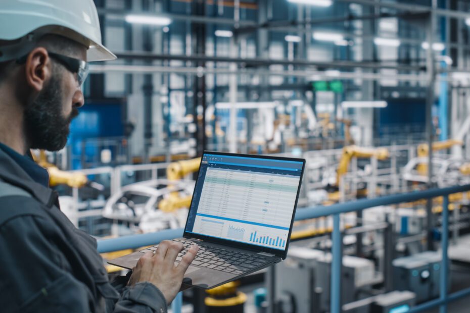 Car Factory Engineer in Work Uniform Using Laptop Computer with