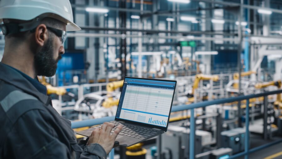 Car Factory Engineer in Work Uniform Using Laptop Computer with